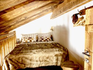 Ein Schlafzimmer mit Holzboden, einem Bett mit karierter Decke und einem Holzschrank mit hängendem Schmuckstück.