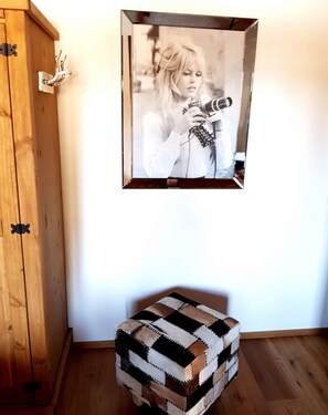 Un mueble de madera con bisagras metálicas, una fotografía enmarcadas en la pared y un reposapiés de cuadros en el suelo.