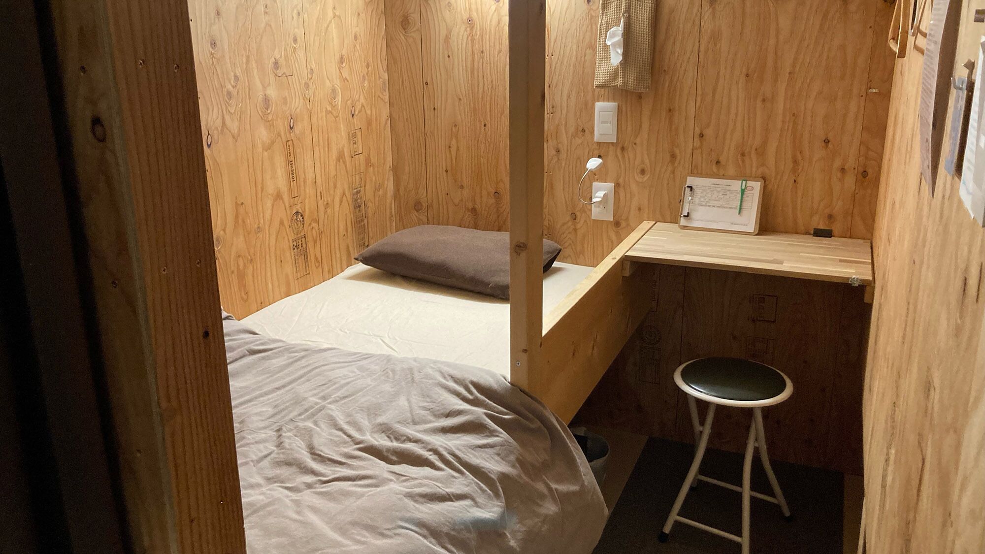 Una habitación pequeña de madera con una cama individual, un escritorio y un taburete.