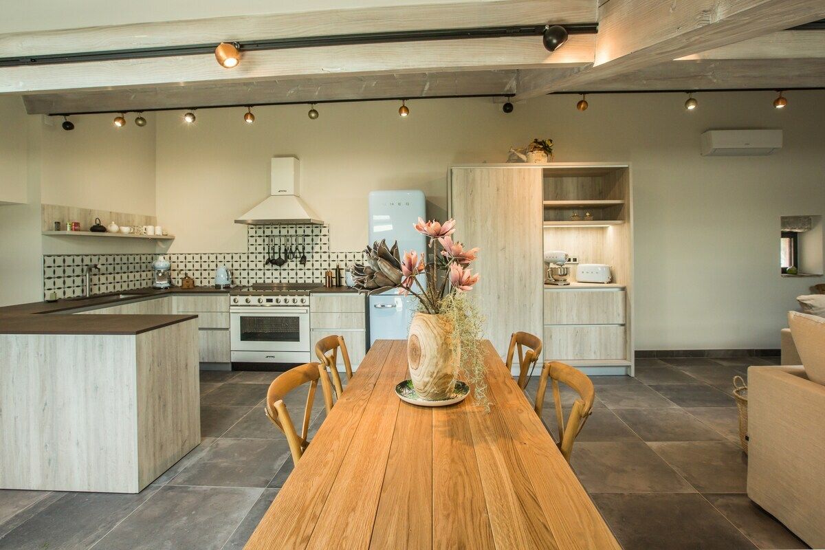 A modern kitchen with a central island, wooden dining table, and a vase with flowers.