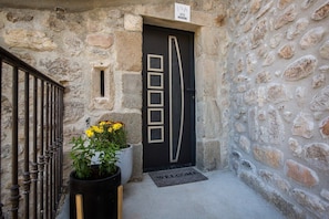 A stone building entrance with a black door, a metal gate, and a welcome mat.