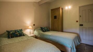 A bedroom with two single beds, a wooden wardrobe, a nightstand with a lamp, and a door with a light switch.