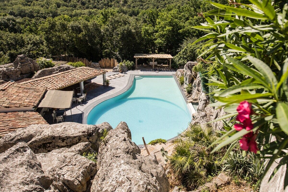 Una piscina de borde curvo, rodeada de rocas y vegetación.