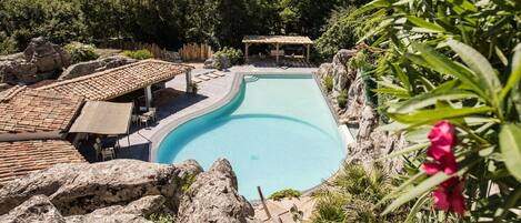 Una piscina de borde curvo, rodeada de rocas y vegetación.