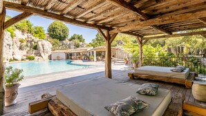 Um deck de madeira com piscina, área de estar ao ar livre e vista para terreno rochoso.