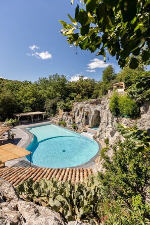A swimming pool with a curved edge, surrounded by a rocky landscape and greenery.