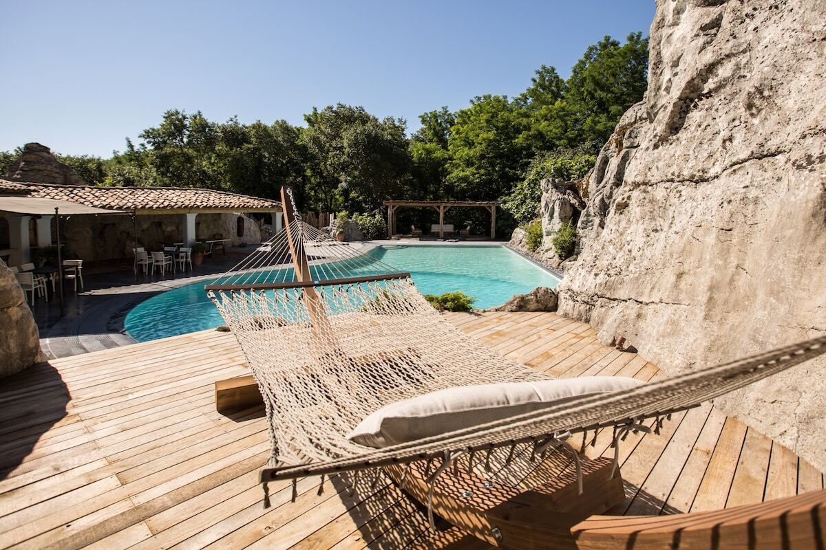 Una terraza de madera con una hamaca, una piscina y un acantilado rocoso de fondo.