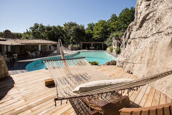 A wooden deck with a hammock, a pool, and a rocky cliff backdrop.