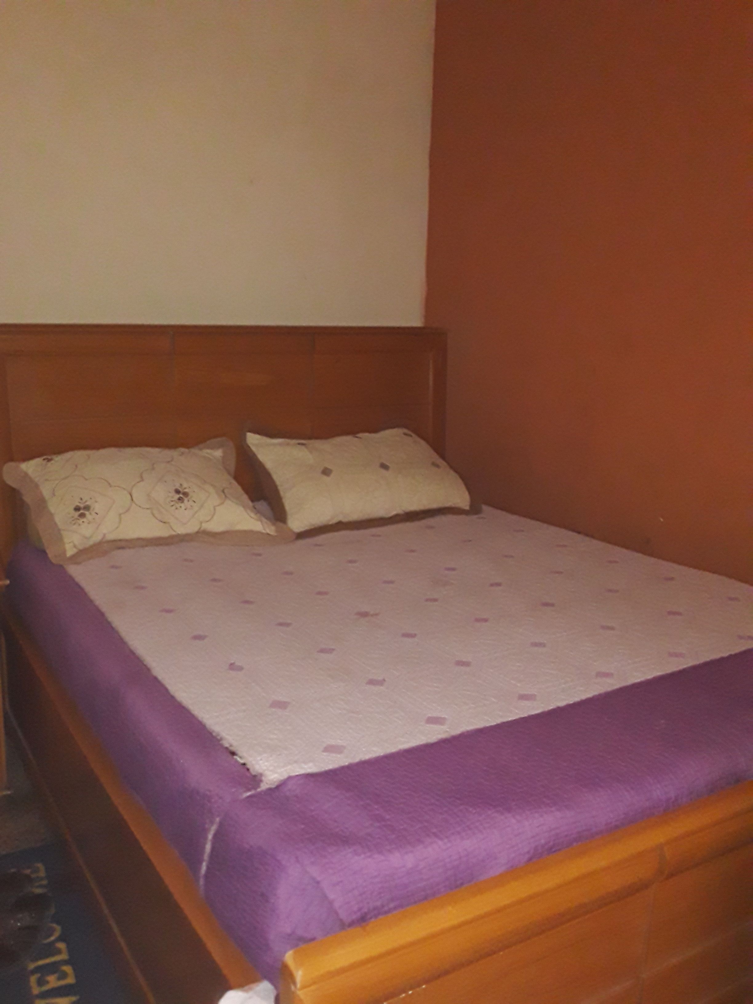 A single bed with a wooden headboard, a purple bedspread, and two pillows with a floral pattern.