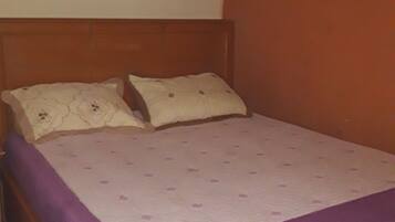 A single bed with a wooden headboard, a purple bedspread, and two pillows with a floral pattern.