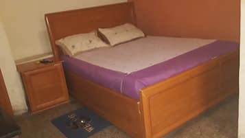 A single-bed room with a wooden headboard, a purple bedspread, and a small bedside table.