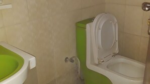 A small bathroom with a green toilet, a white sink, and beige tiled walls.