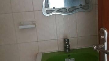A bathroom with a white pedestal sink, a green basin, and a wall-mounted mirror with a decorative frame.