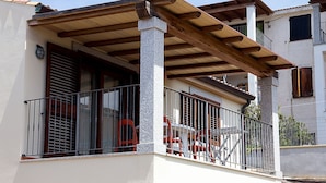 Een gebouw met twee verdiepingen, met een balkon dat een houten pergola, een metalen hekwerk en rode stoelen heeft.