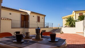 Une terrasse extérieure avec une table dressée pour deux personnes, une machine à café et une vue sur un immeuble doté d’un balcon.