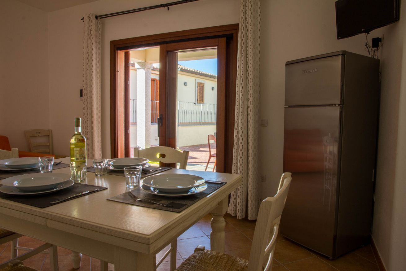 Un comedor con una mesa lista para cuatro, un refrigerador y vistas al balcón exterior.