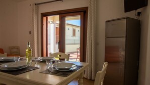 Un coin repas avec une table dressée pour quatre personnes, un réfrigérateur et une vue sur le balcon extérieur.