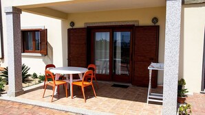 An outdoor patio with a round table and four orange chairs, a wooden door, and a small potted plant. - SMART GROUND (badesi)