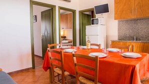 Comedor con mesa dispuesta para cuatro, microondas y televisor sobre los armarios.