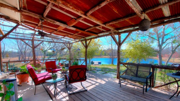 A covered outdoor patio with wooden flooring, metal-framed chairs, and potted plants. - Mesquite Creek Farmhouse (New Braunfels)