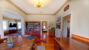 A spacious living room with a wooden dining table, a bookshelf, and a television mounted on the wall. - Mesquite Creek Farmhouse (New Braunfels)