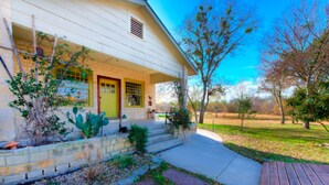 A house with a front porch, a stone retaining wall, and a wooden deck. - Mesquite Creek Farmhouse (New Braunfels)