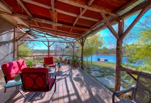 A covered outdoor seating area with red chairs and a table, overlooking a body of water.