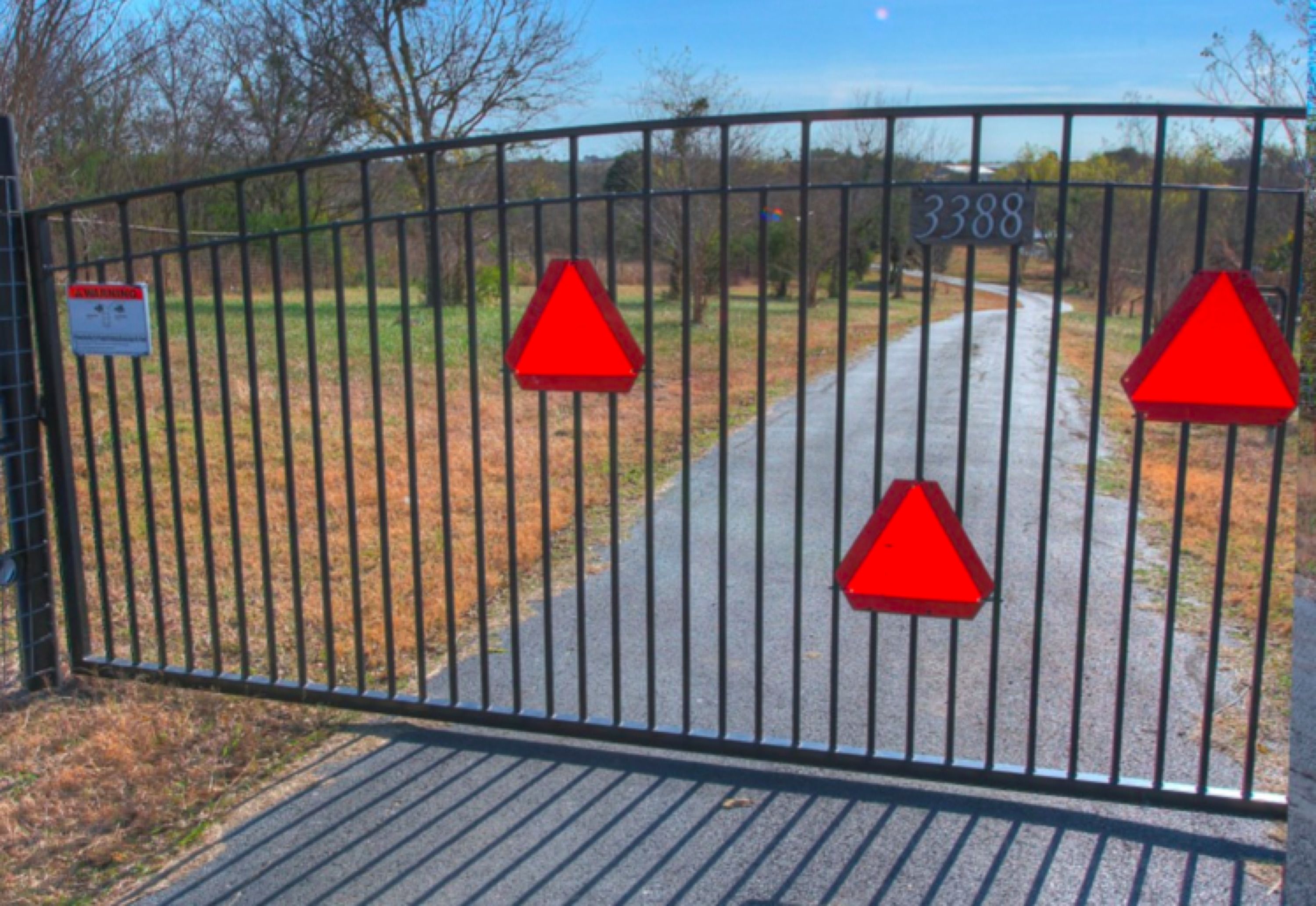 A gated entrance with a metal fence and three red triangular warning signs.