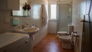 Ein Badezimmer mit Waschmaschine, zwei Waschbecken, Toilette und einer Duschkabine aus Glas.