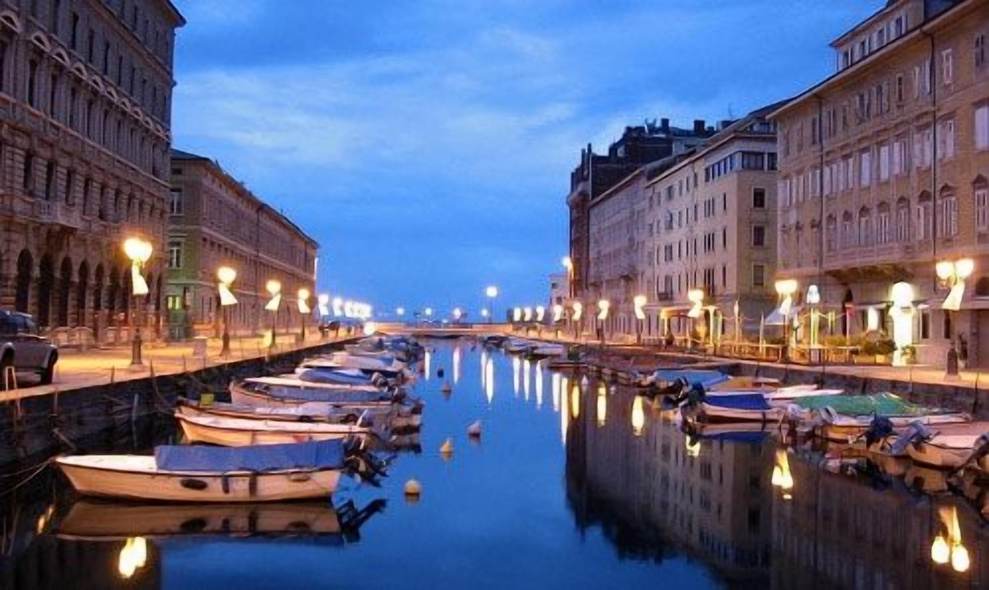 A canal lined with boats and buildings, reflecting the lights.