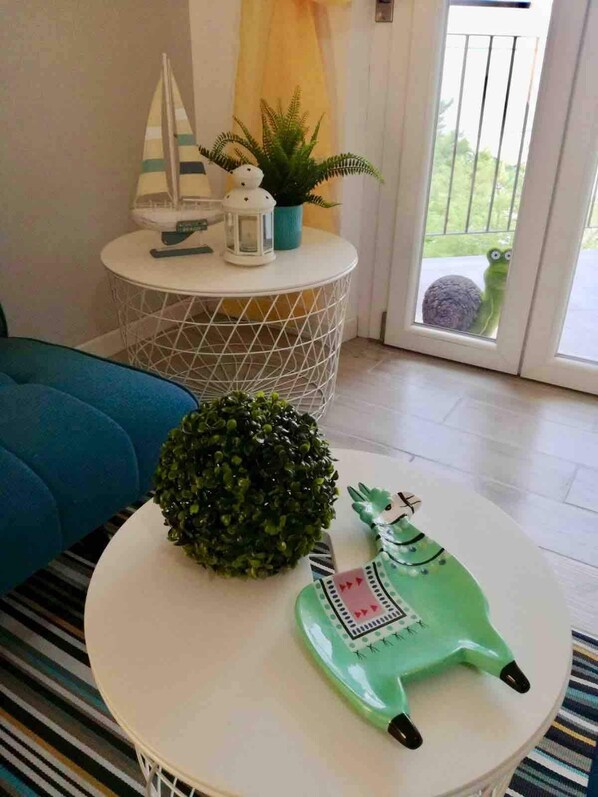 A room with a round white table, a blue sofa, a small white table with decorative items, and a view through a glass door. - La Finestra sul mare (Marina Julia, Monfalcone,Italy)