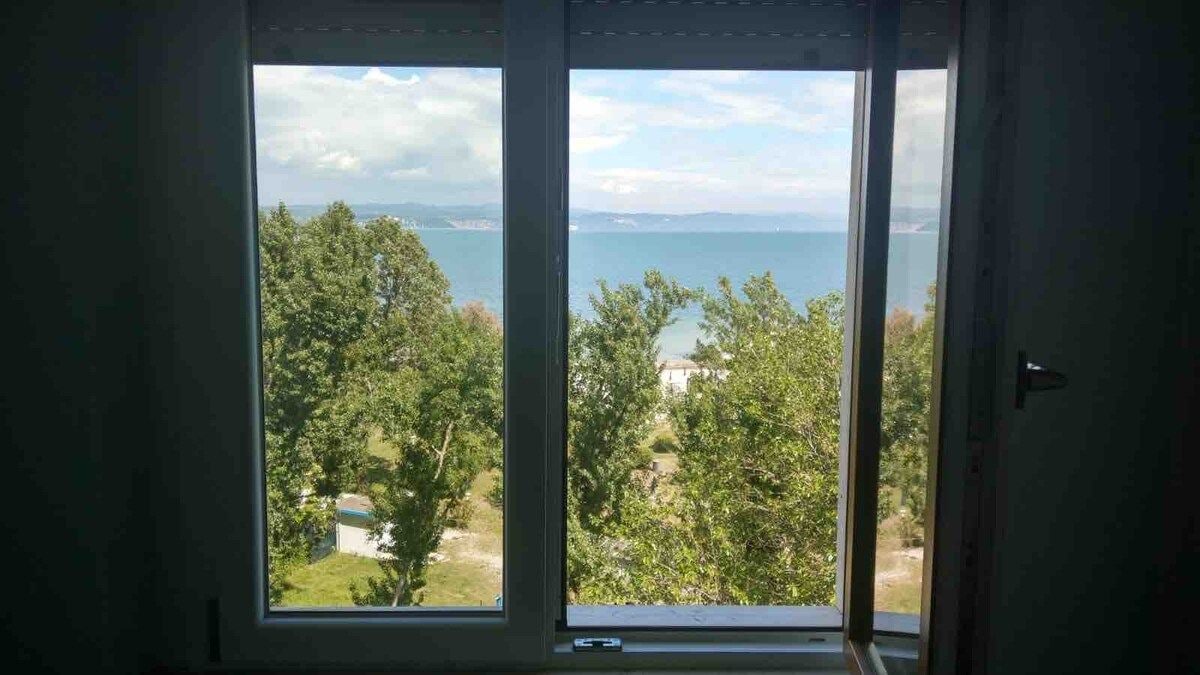 A room with a large window offering a view of a body of water and greenery.
