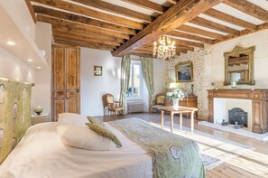 A bedroom with a bed, wooden beams, a chandelier, a fireplace, and a stone wall. - Manoir 5 épis 14 pers, park, Normandy (Amayé-Sur-Orne)