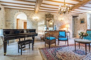 A rustic room with a grand piano, wooden chairs, a chandelier, and a stone wall. - Manoir 5 épis 14 pers, park, Normandy (Amayé-Sur-Orne)
