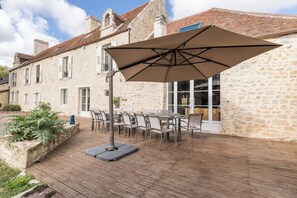 A stone building with a patio area featuring outdoor seating and a large umbrella. - Manoir 5 épis 14 pers, park, Normandy (Amayé-Sur-Orne)