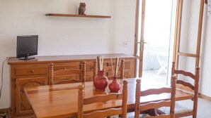 A room with a wooden dining table, chairs, a wooden desk with a computer monitor, and a window with a view of the outdoors. - APPARTAMENTO LA PILA - APPARTAMENTO LA PILA (Campo nell'Elba)