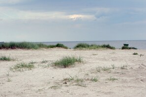 Een zanderig strand met weinig gras en een gebouw in de verte.