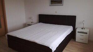 Une chambre avec un grand lit, deux tables de chevet, une commode, un tableau encadré au mur et un plancher en bois.