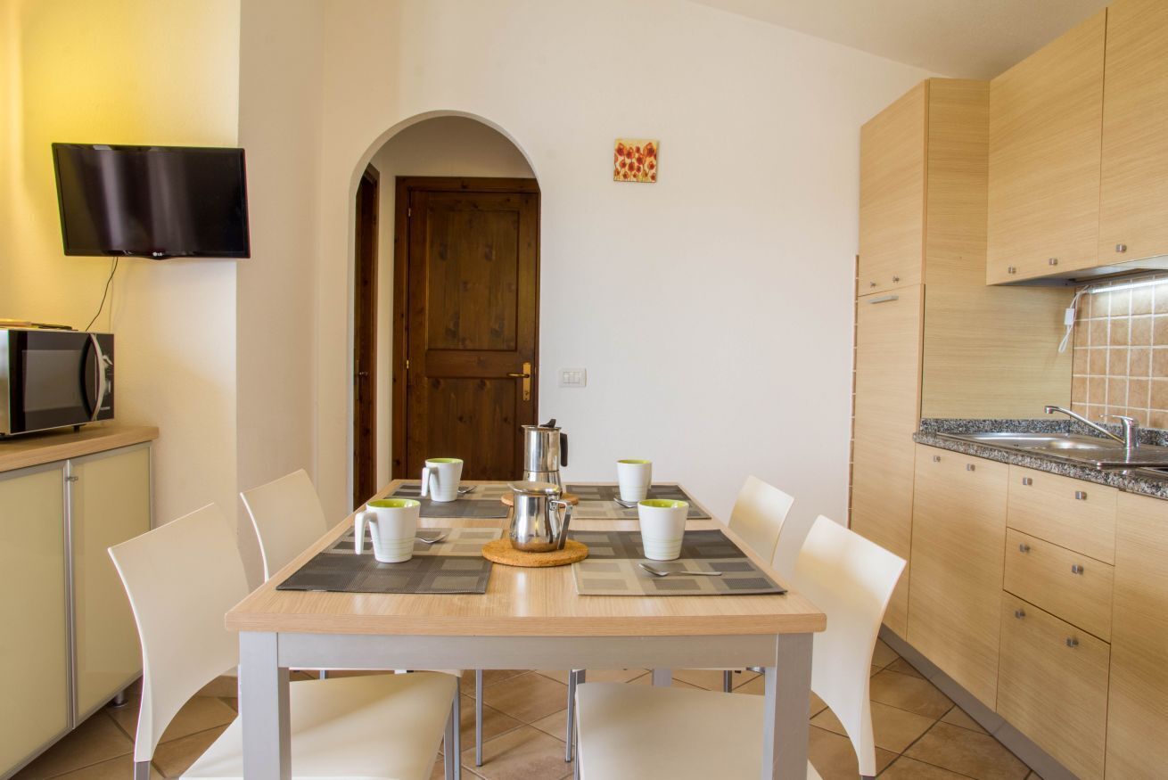 Une cuisine moderne équipée d’une table à manger pour quatre personnes, d’une machine à café et d’un téléviseur à écran plat fixé au mur.