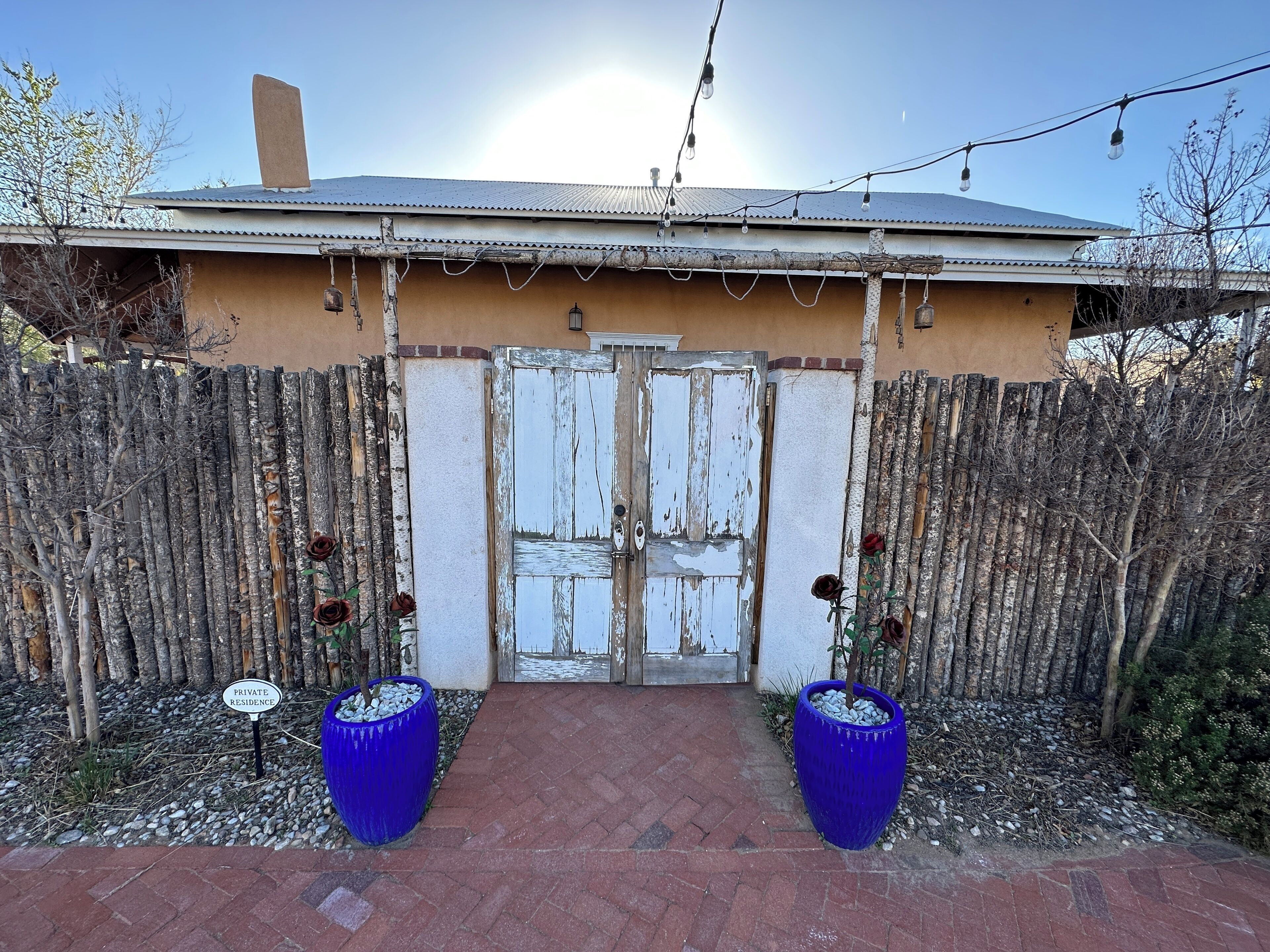 A gated entrance with a rustic wooden fence, a weathered white door, and two large blue planters with roses.