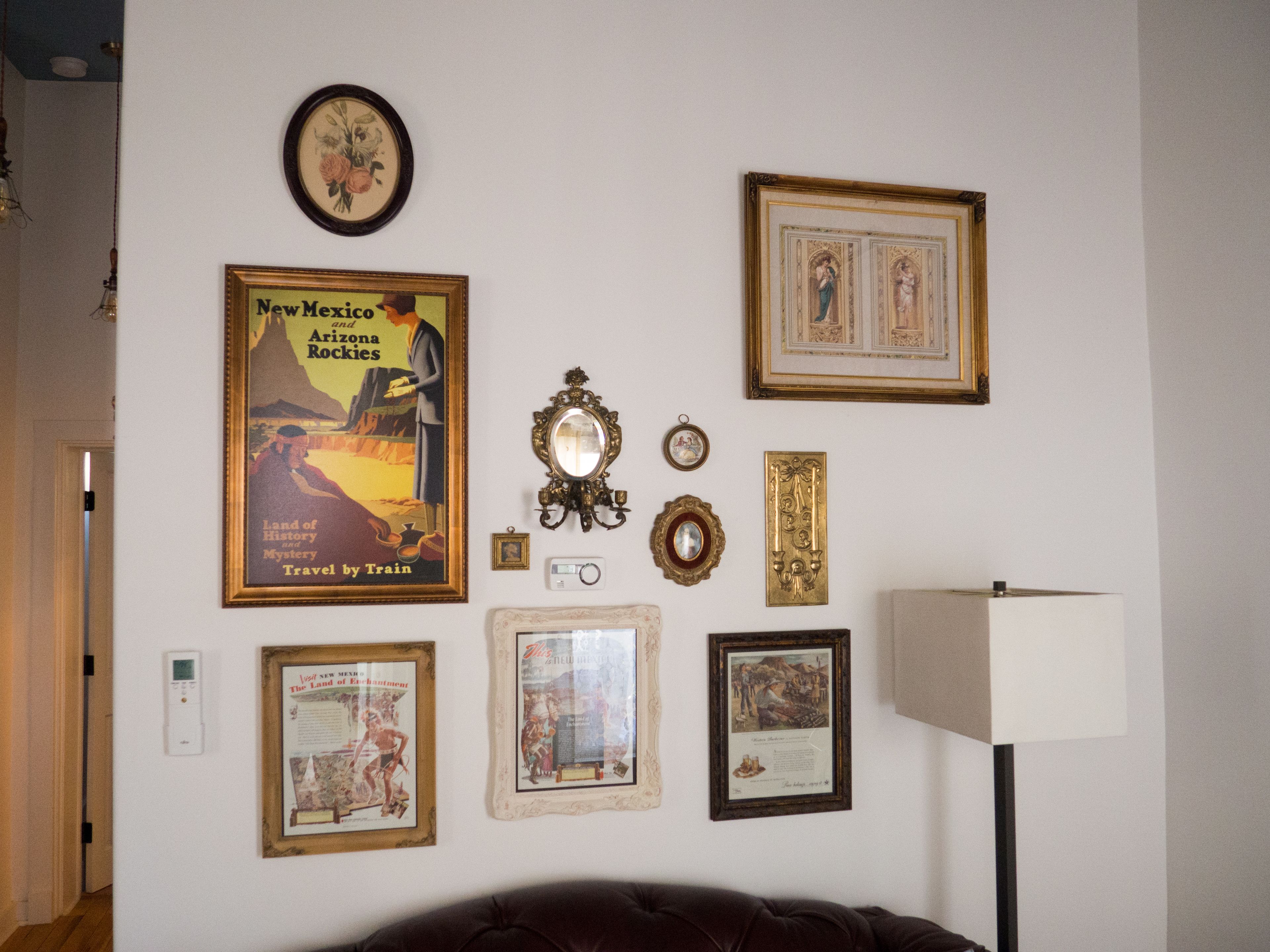 A wall with various framed items including travel posters and decorative mirrors.
