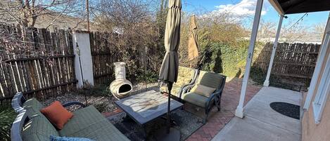 A covered patio with two cushioned chairs, a table, and an umbrella.