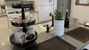 Une cuisine avec des armoires blanches, un four à micro-ondes, un réfrigérateur, une cuisinière et un présentoir à trois niveaux contenant des aliments.