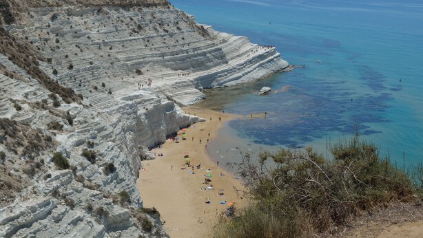 Ein Küstenstrand mit geschichteten weißen Felsen und klarem, blauem Wasser.