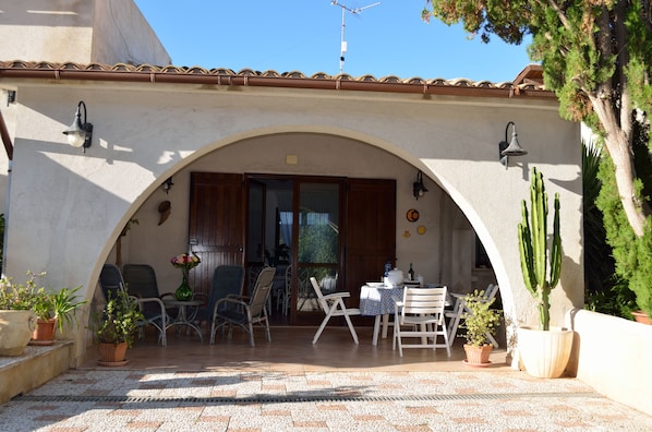 Un espacio al aire libre con patio, piso de baldosas, varias sillas, una mesa y macetas con plantas.