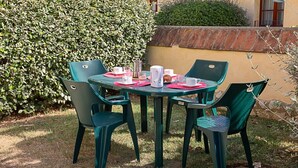 Una mesa al aire libre con cuatro sillas, una jarrón, tazas y un plato.