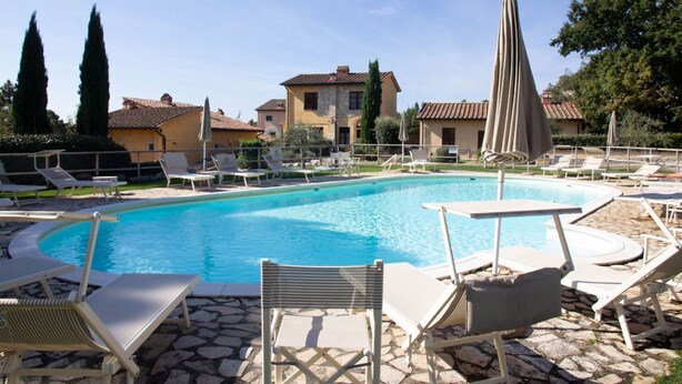 Una piscina con sillas de descanso y sombrillas, rodeada de baldosas de piedra y edificios.