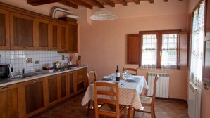 Una cocina con armarios de madera, salpicadero de azulejos, una mesa de comedor con sillas y una ventana con cortinas.