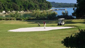 Campo de golf con un búnker de arena, un carrito de golf y una persona a punto de hacer un putt.