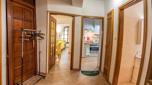 Un pasillo con una puerta de madera, un perchero con objetos colgando y un tapete de bienvenida.